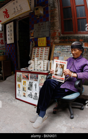 Eine sehr nette schöne und elegante chinesische Dame im Alter von 93 Jahren sitzt vor ihrem Buchladen in Guangzhou mit Mao-Propaganda. Stockfoto