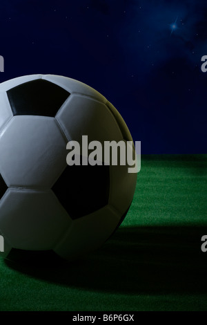 Studioaufnahme von einem schwarzen und weißen Fußball Schuss aus einem niedrigen Winkel mit grünem Rasen und ein Nachthimmel mit Sternen Stockfoto