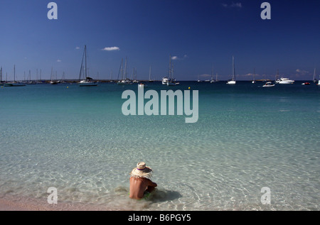 Junger Mann mit einem Strohhut sitzen am Strand von Espalmador, auf den Balearischen Inseln, Blick auf den Horizont Stockfoto