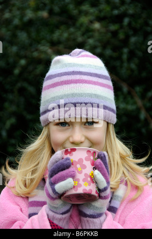 Porträt der ein kleines Mädchen lächelnd und warme Kleidung mit einer Wollmütze und trinken aus einem Becher Stockfoto