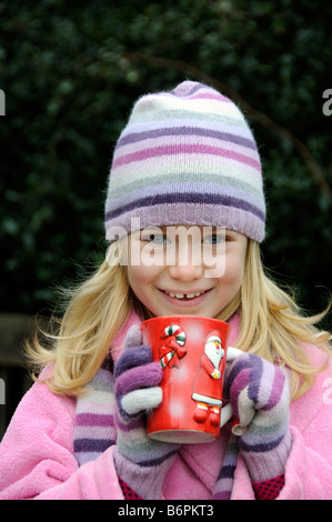 Porträt der ein kleines Mädchen lächelnd und warme Kleidung mit einer Wollmütze und trinken aus einem Becher Stockfoto