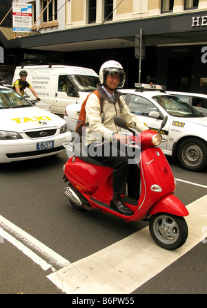 Ein Mann fährt einen roten Vespa Motorscooter im Stadtverkehr Stockfoto