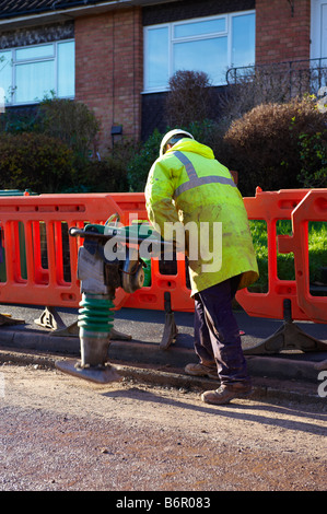 Arbeiter mit heavy-Duty-Pfünder, Pfund Kies in Straße nach der Verlegung, elektrische Verkabelung Stockfoto