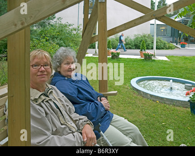 mittelalterlichen Frau besuchen ihre Mutter im Heim für alte Leute sitzen im Garten mit einem chat Stockfoto