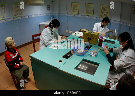 Young Asian kaukasischen jungen erwartet Immunisierung Schüsse in Guangzhou Guangdong China chinesische Krankenschwestern Ärzte sind an Tisch sitzen Stockfoto