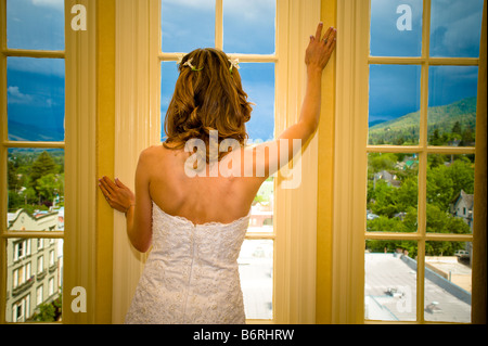 Braut stehen in einem Fenster beobachten, wie Gewitterwolken außerhalb wirbeln Stockfoto