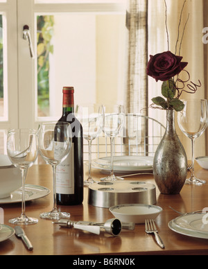 Nahaufnahme der Flasche Wein und Gläser mit Gedeck am Esstisch mit roter Rose in Metall vase Stockfoto