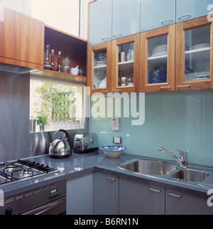 Holzwand Schränke oben Glas Spritzschutz in modernen Küche mit Chrom Wasserkocher und Toaster auf graue Arbeitsplatte unter Fenster Stockfoto