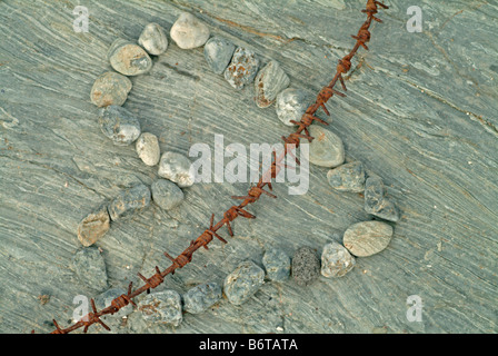 Herz aus Steinen mit rostigen Stacheldraht auf grauem Stein gemacht Stockfoto