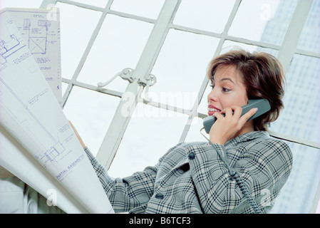 Junge Frau mit Blaupausen, die auf einem Festnetztelefon sprechen, USA 1999 Stockfoto