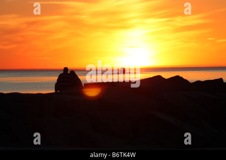 Paar, sitzen auf den Felsen in New Buffalo Michigan mit Blick auf Lake Michigan bei Sonnenuntergang Stockfoto