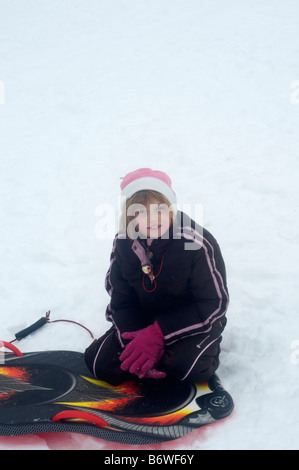 Junges Mädchen kniend auf ihrem Schlitten. Stockfoto