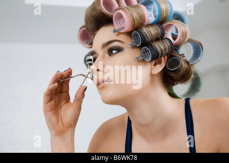 Modell in Lockenwickler mit Wimpernzange Stockfoto