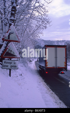 LKW Reisen durch Winterschnee vorbei Warnung Wegweiser der scharfen Kurve und steilen Hügel vor Sutton Bank Yorkshire UK Stockfoto