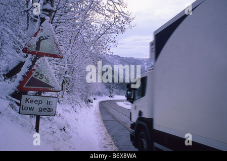 LKW vorbei Schnee bedeckt Straßenschilder Warnung vor steilen Hügel und scharfe Biegung bei Sutton Bank in der Nähe von Thirsk im Winter Yorkshire UK Stockfoto