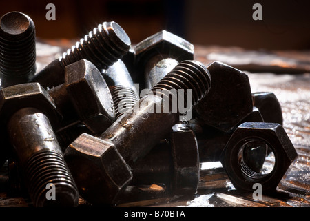 Zufällige künstlerische Haufen von Gewindebolzen und eine Sechskantmutter auf ein Stahlblech, Hintergrundbeleuchtung. Stockfoto