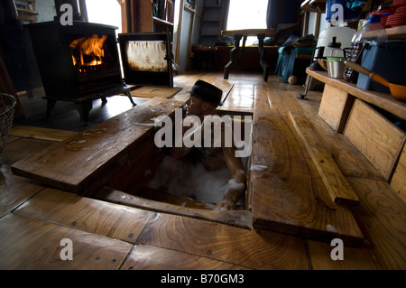 Mann baden in seine Hand aus Holz Kabine, in der Badewanne, unter der Küche, Boden und Wasser erhitzt auf Holz befeuerten Herd eingestellt ist. Off Grid leben. Stockfoto