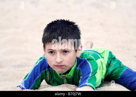 Ein kleiner Junge liegt im Sand am Strand an einem warmen Sommertag. Stockfoto