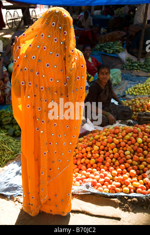 Eine Frau trägt einen Schleier und orangefarbenen Sari besucht einen Marktstand in Indien. Stockfoto