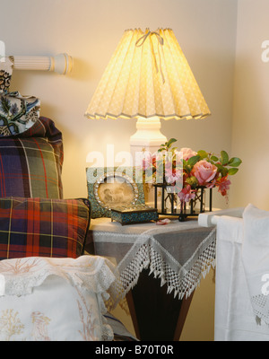 Beleuchtete Lampe mit rosa Rosen in Vase auf Nachttisch mit Lace-Tuch in der Ecke des Schlafzimmers Stockfoto