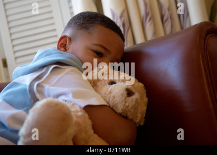 Ein kleiner Junge hält einen Teddybären suchen Angst saß auf einem Stuhl Stockfoto