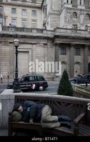 Ein Obdachloser, der bei kaltem Wetter auf einer Bank schläft, gegenüber der Bank of England in der Threadneedle Street, London, Großbritannien. Stockfoto