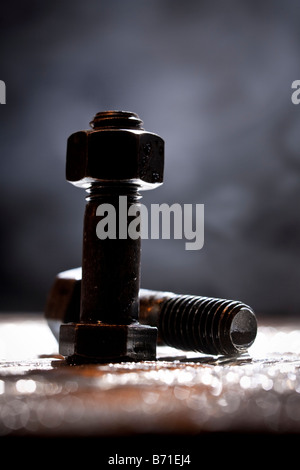 Zufällige künstlerische Haufen von Gewindebolzen und eine Sechskantmutter auf ein Stahlblech, Hintergrundbeleuchtung. Stockfoto