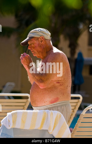 Palm Beach Shores, Sonnenbrille Pool Reife große behäbige älterer Mann in kurzen Hosen Baden Stämme & Baseball-Cap aufsetzt. Stockfoto