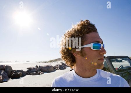 Junger Mann mit Sonnenbrille am Strand neben dem jeep Stockfoto