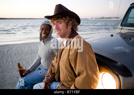 Junge interracial Pärchen sitzt auf Jeep am Strand trinken Bier Stockfoto