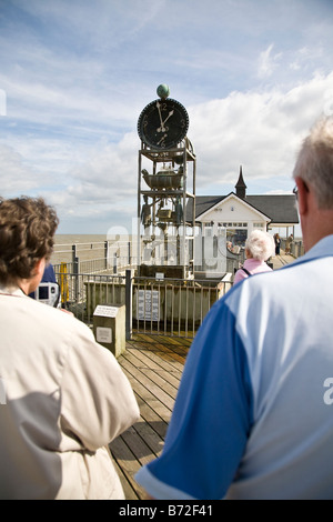 Älteres Ehepaar, mit dem Rücken zur Kamera und etwas abgeschnitten von Rahmen, Blick auf den berühmten Southwold Pier Wetterfahne. Stockfoto