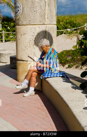 South Beach Miami, Lummus Park, große ältere alten grauen Haaren in Badesachen & bunte Top sitzen in der Sonne lesen Stockfoto