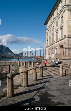 Palazzo Borromeo auf Isola Bella mit Blick auf die Alpen und die Isola dei Pescatori, Lago Maggiore, Italien. Paar, sitzen auf den Stufen. Stockfoto