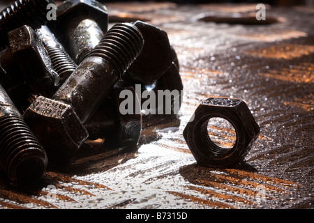 Zufällige künstlerische Haufen von Gewindebolzen und eine Sechskantmutter auf ein Stahlblech, Hintergrundbeleuchtung, Stockfoto