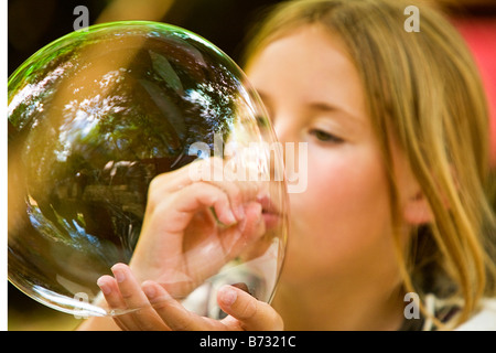 Bild von einem jungen blonden Mädchen bläst eine riesige Seifenblase, die sie in ihren Händen balanciert Stockfoto