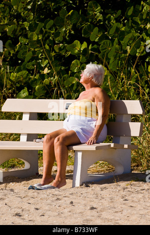 Palm Beach Shores, Florida, Reife große grauen Haaren Seniorin schlafend im Sonne Sonnenbaden auf Bank auf Sand am Strand Stockfoto