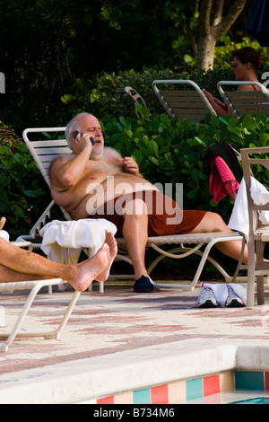 Palm Beach Shores, Schwimmbad, grauen Haaren großen mittleren Alter Mann auf der Liege im Schwimmen Shorts Gespräche über Handy Stockfoto