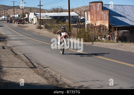 Ein Dirt Bike Motorcyle Fahrer macht einen Wheelie in der Hauptstraße Randsburg Kaliforniens Mojave-Wüste Stadt, die Biker anzieht. Stockfoto