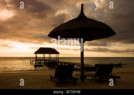 Sonnenuntergang am Indischen Ozean auf Mauritius mit Strandliegen und Schirm Regenschirm und Holzsteg Stockfoto