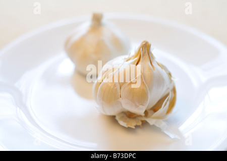 2 Knoblauch Zwiebeln mit Nelken ausgesetzt, 1 geschälte und 1 ungeschälte auf weißen Teller Stockfoto