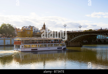 Sevilla Spanien Ausflugsschiff fährt unter der Puente de Triana oder Puente de Isabell II auf dem Fluss Guadalquivir Stockfoto