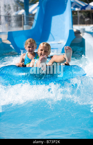 Porträt von Mädchen Rutschen Wasserrutsche zusammen auf Innertube im Wasserpark Stockfoto