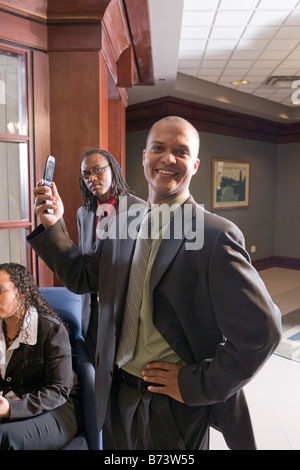 Afrikanisch-amerikanischer Geschäftsmann lächelnd und Handy hochhalten Stockfoto