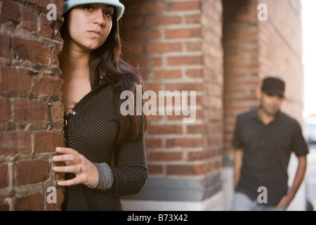 Junge Frau Blick hinter Mauer, Man nähert sich im Hintergrund Stockfoto