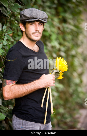 Junger Mann stand vor Efeu bedeckte Wand, mit gelben Sonnenblumen Stockfoto