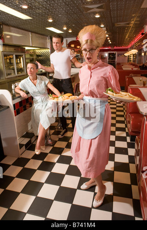 Paar streiten, während Kellnerin Teller mit Essen im Diner Stil der 1950er serviert Stockfoto