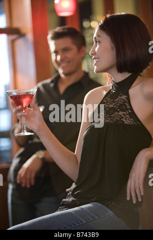 Hübsche junge Frau, die Drink an der bar Mann im Hintergrund beobachtet Stockfoto