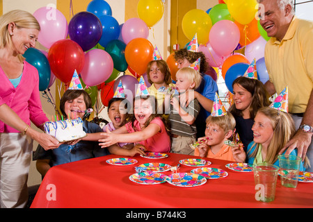 Gruppe von Kindern, die Spaß an der Geburtstagsfeier, Mutter hält Kuchen Stockfoto