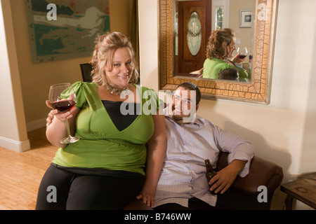 Paar mit Getränken auf Sessel im Wohnzimmer sitzt Stockfoto