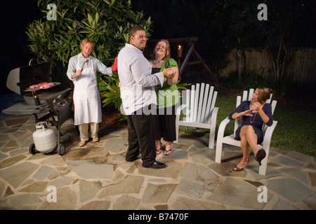 Vier Freunde, die Spaß Grillen Steaks auf Hinterhof Terrasse Stockfoto